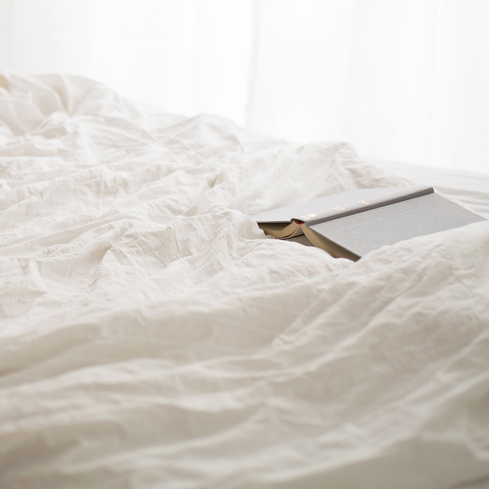 A grey book sits folded open on a fluffy duvet. ATJ Spotify playlist for Balance.