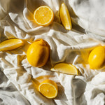 Full lemons and lemon wedges sit on a rumpled white bedsheet. ATJ Spotify playlist for Juicy Citrus.