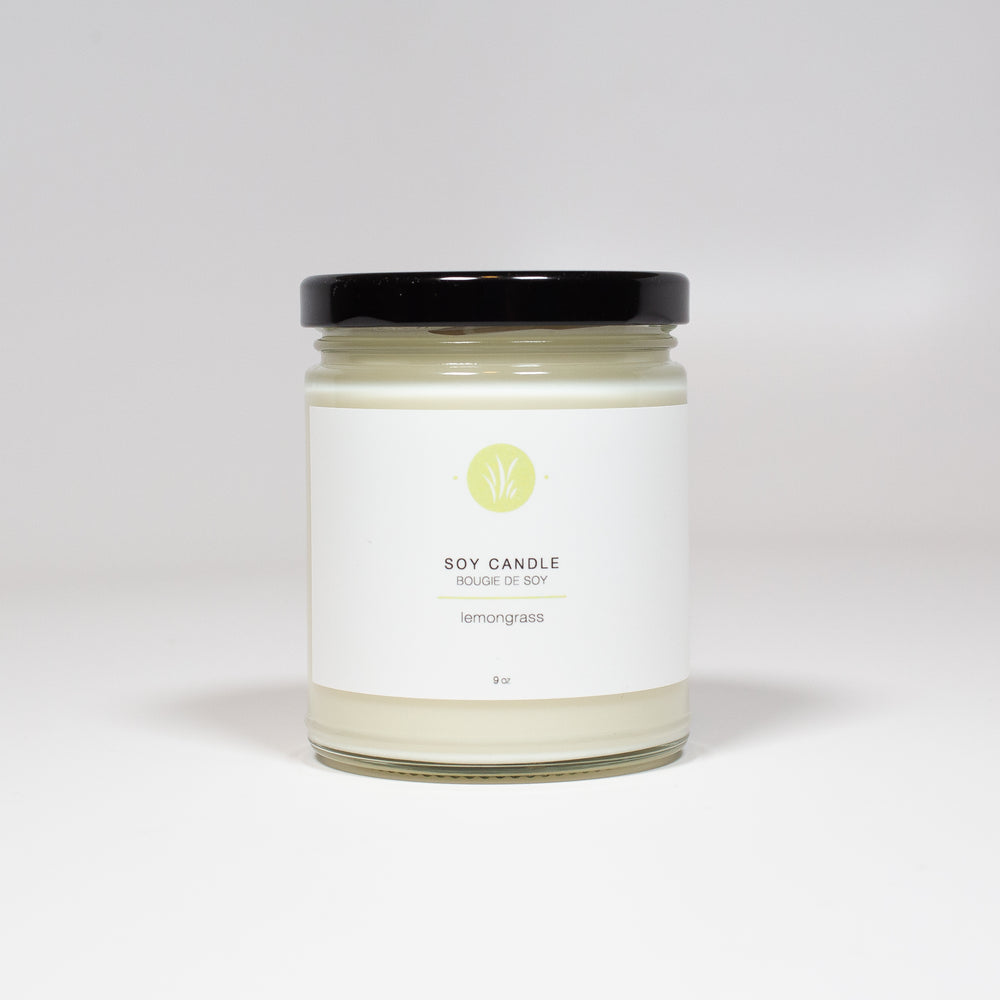 A clear glass jar with a black lid has a label that reads "Soy Candle: Lemongrass". The label is white and green.